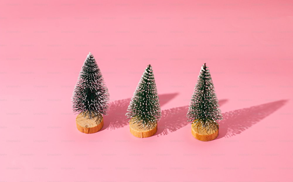 Tres pequeños árboles de Navidad sentados sobre una superficie rosa