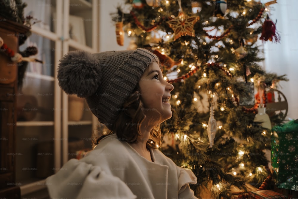 クリスマスツリーの前に立つ帽子をかぶった女性