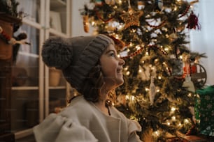 a woman wearing a hat standing in front of a christmas tree