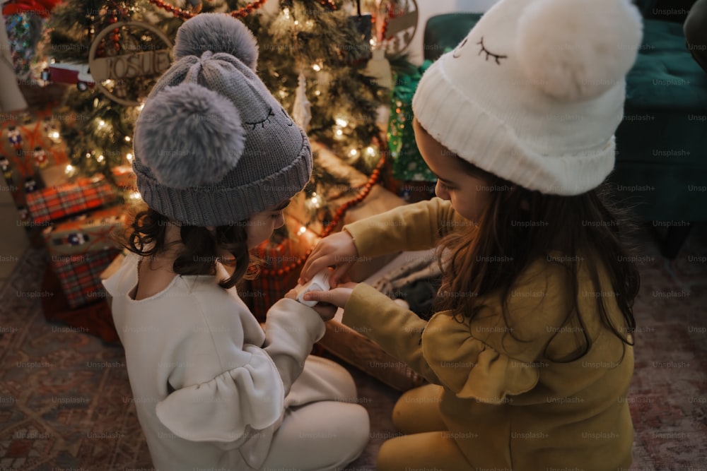 two little girls sitting in front of a christmas tree