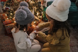 two little girls sitting in front of a christmas tree
