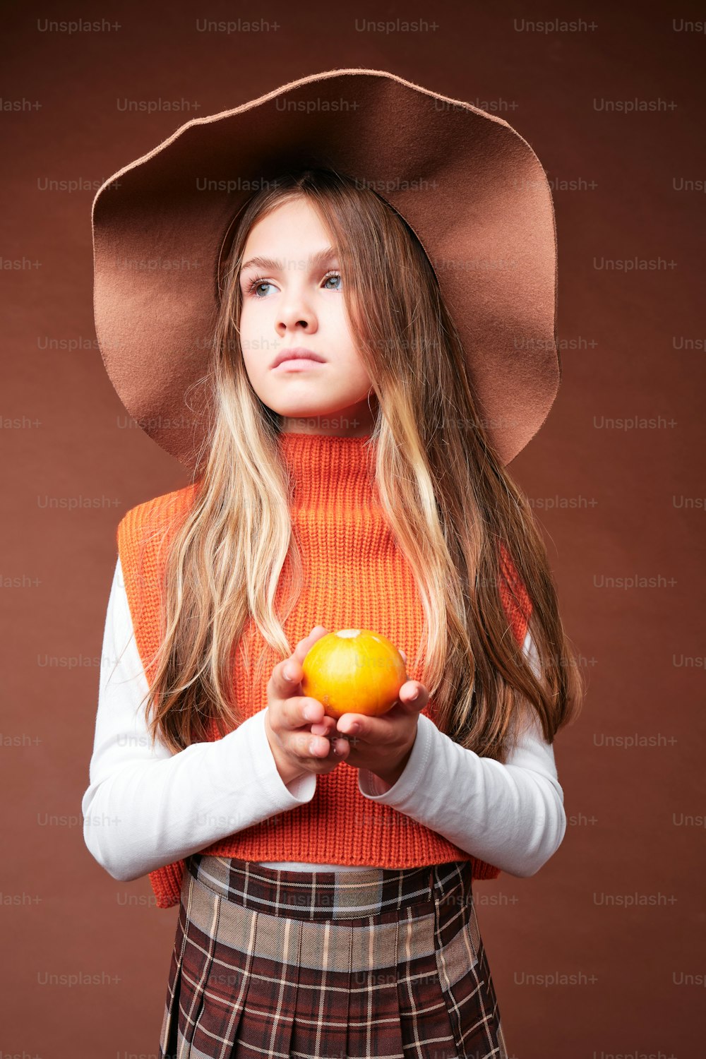 a young girl wearing a cowboy hat holding an orange