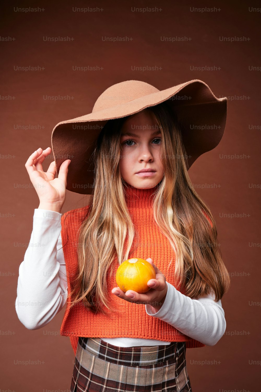 eine Frau, die einen Hut trägt und eine Orange hält