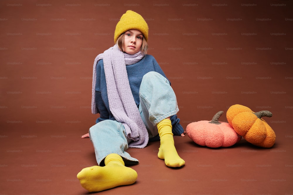 a woman sitting on the ground next to two knitted pumpkins