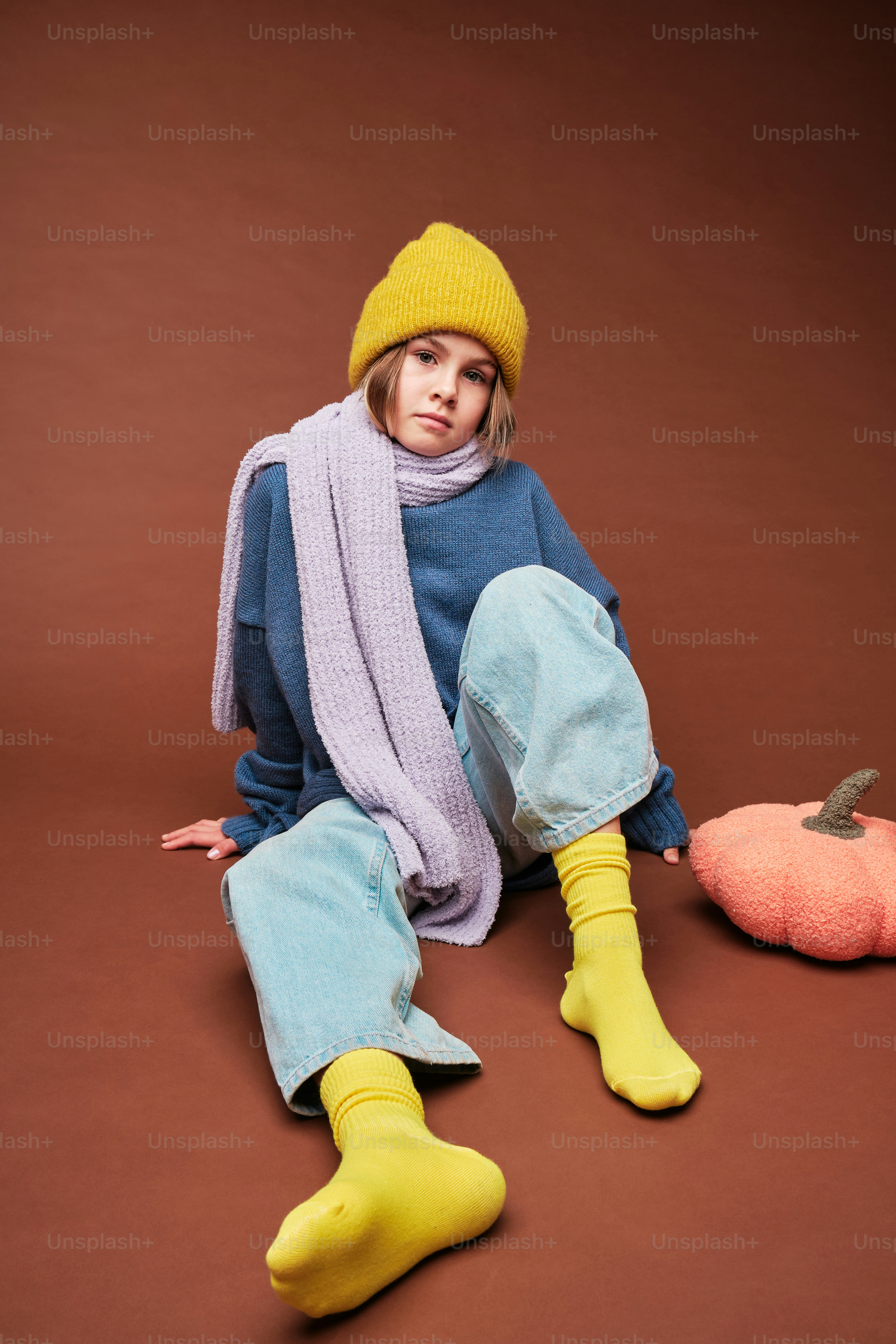 a woman sitting on the ground wearing a yellow hat and scarf