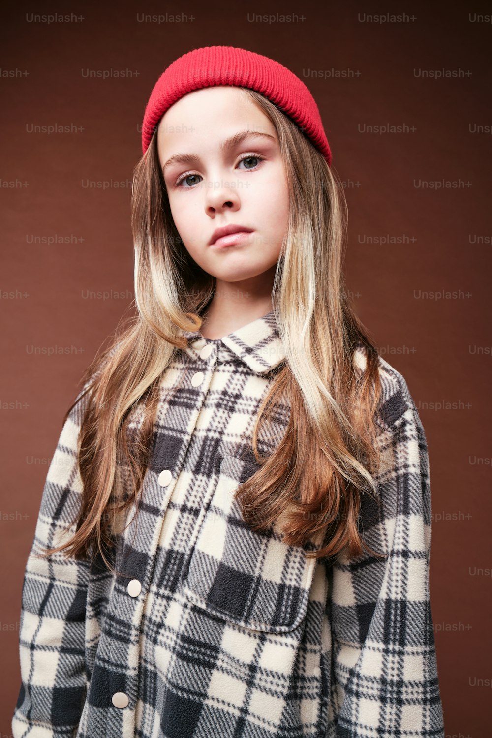 a young girl wearing a plaid coat and a red beanie