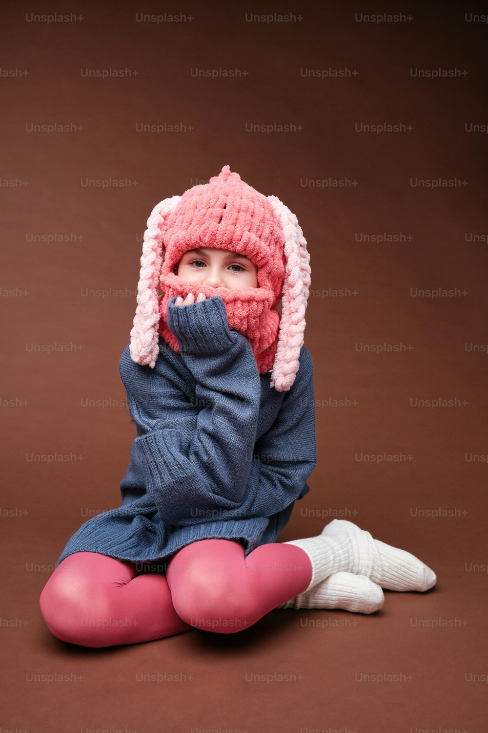 a little girl sitting on the ground wearing a pink hat