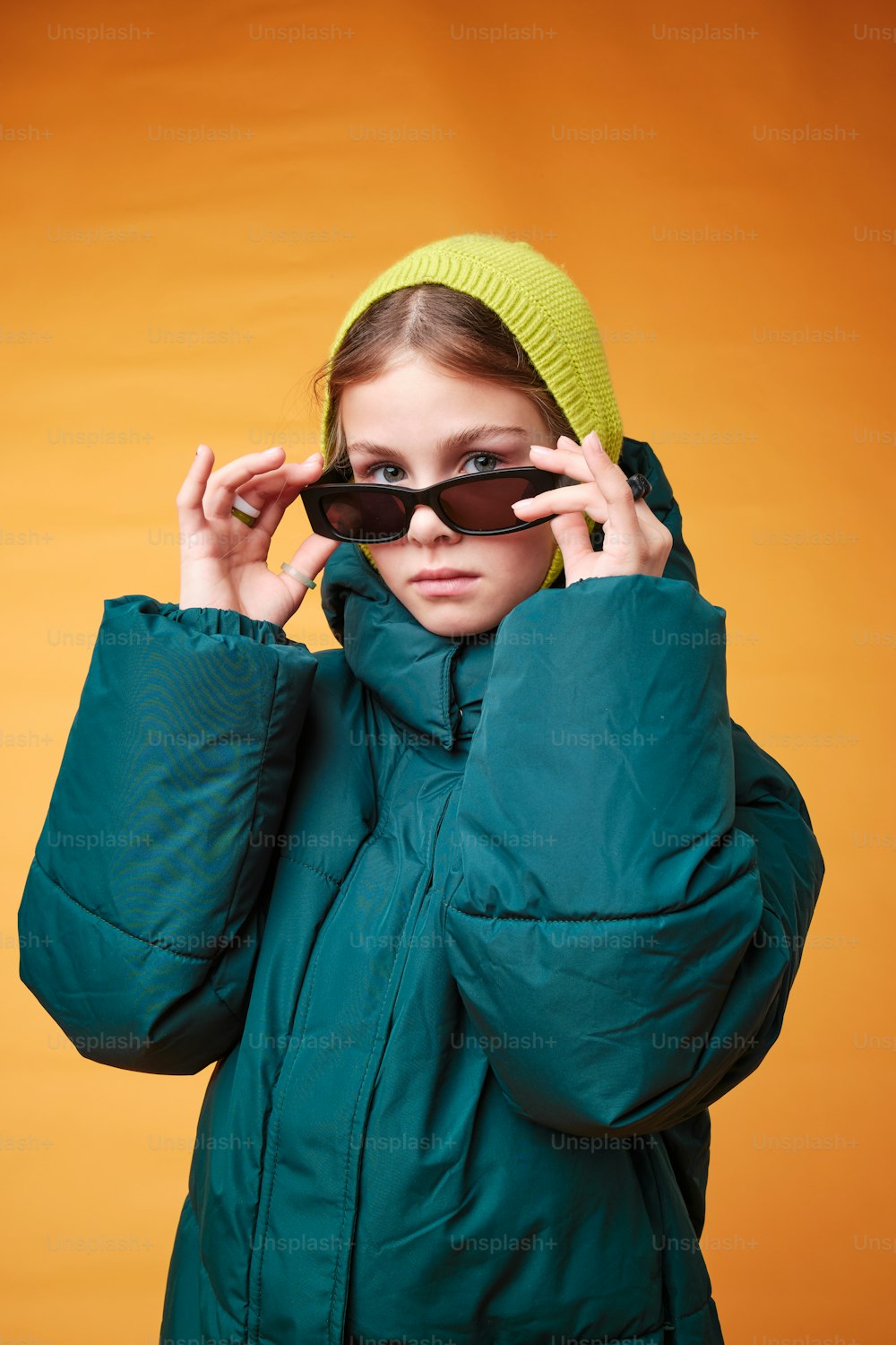 a girl in a green jacket holding a pair of sunglasses