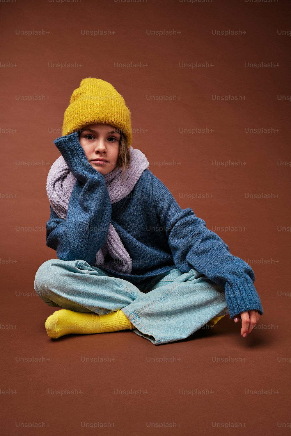 a little girl sitting on the ground wearing a yellow hat