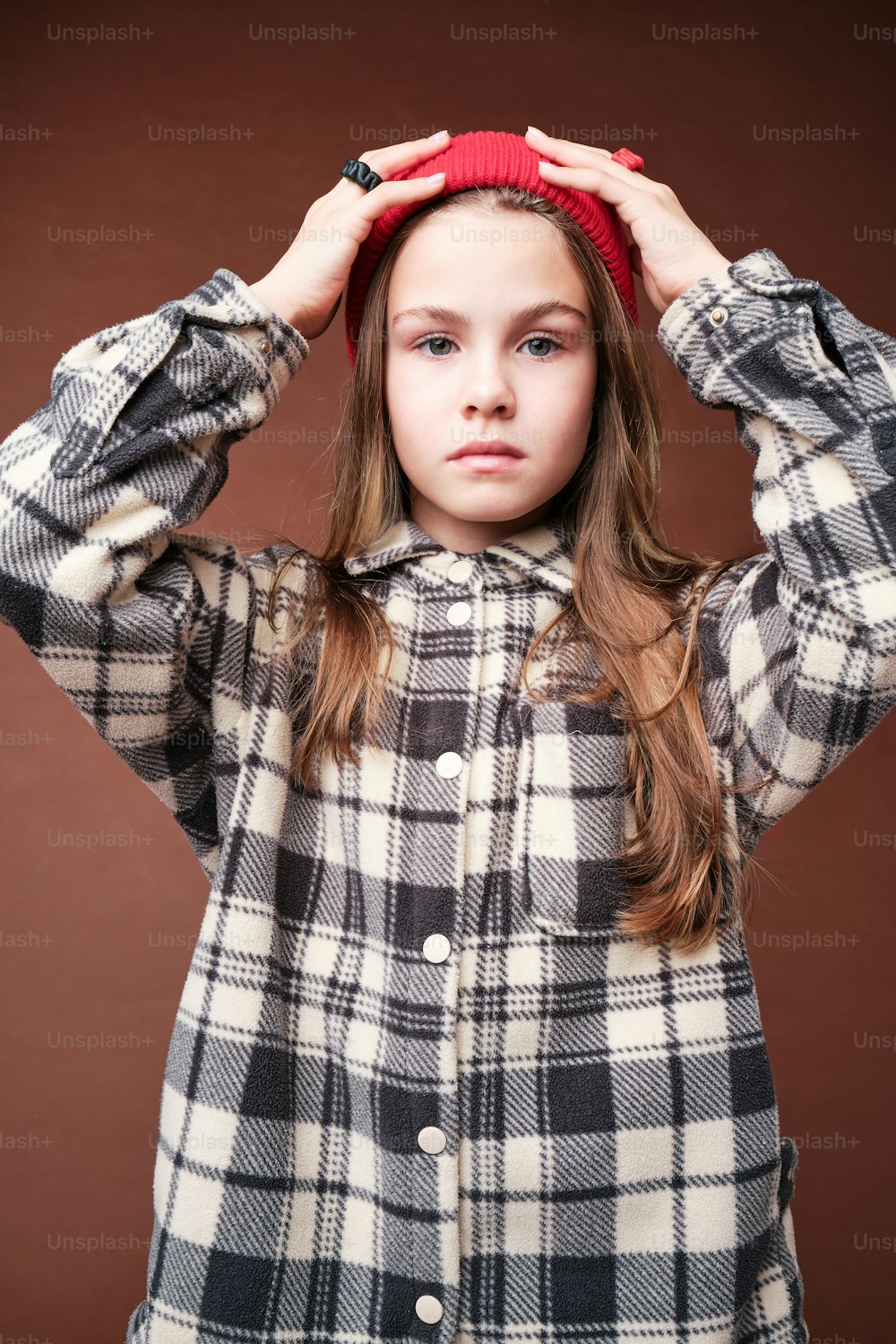 a young girl wearing a plaid jacket and a red beanie