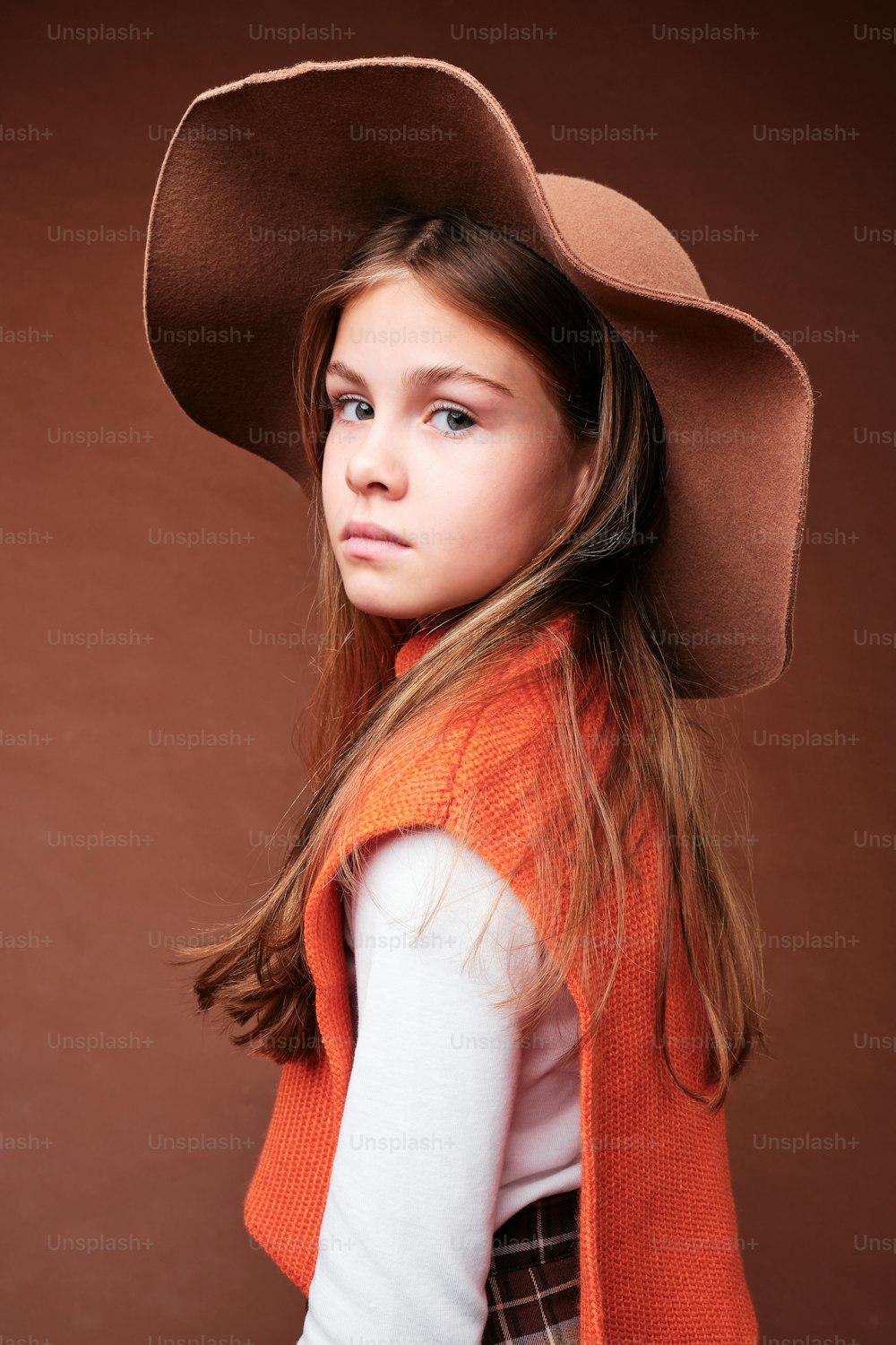 a young girl wearing a brown hat and vest