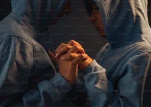 a man in a blue hoodie is holding his hands together