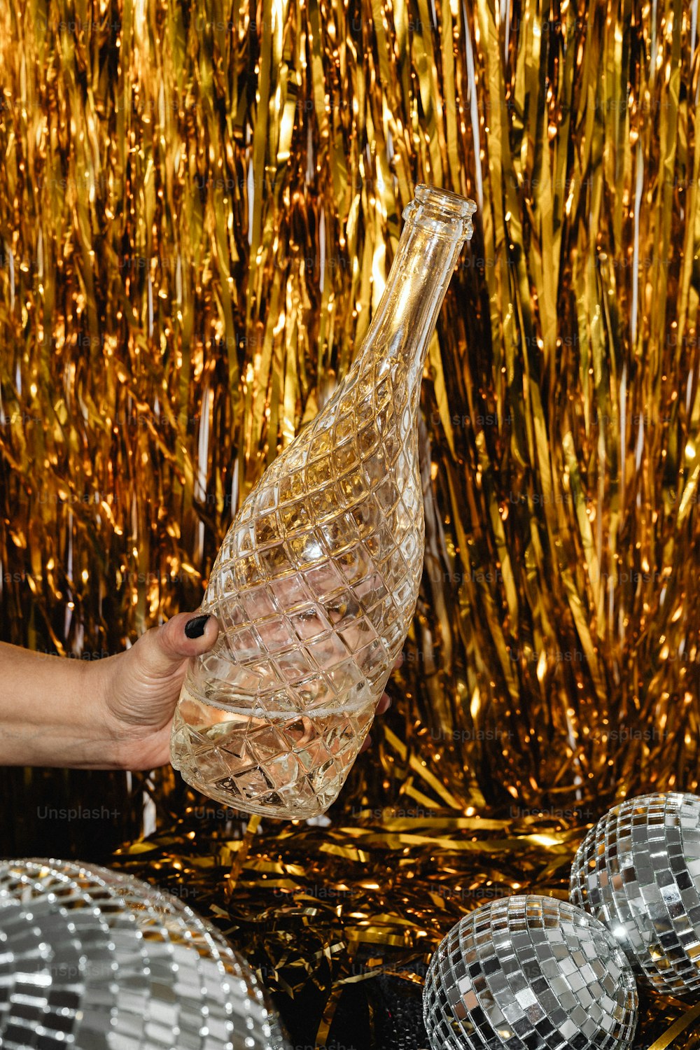 una persona sosteniendo una botella de vidrio frente a bolas de discoteca