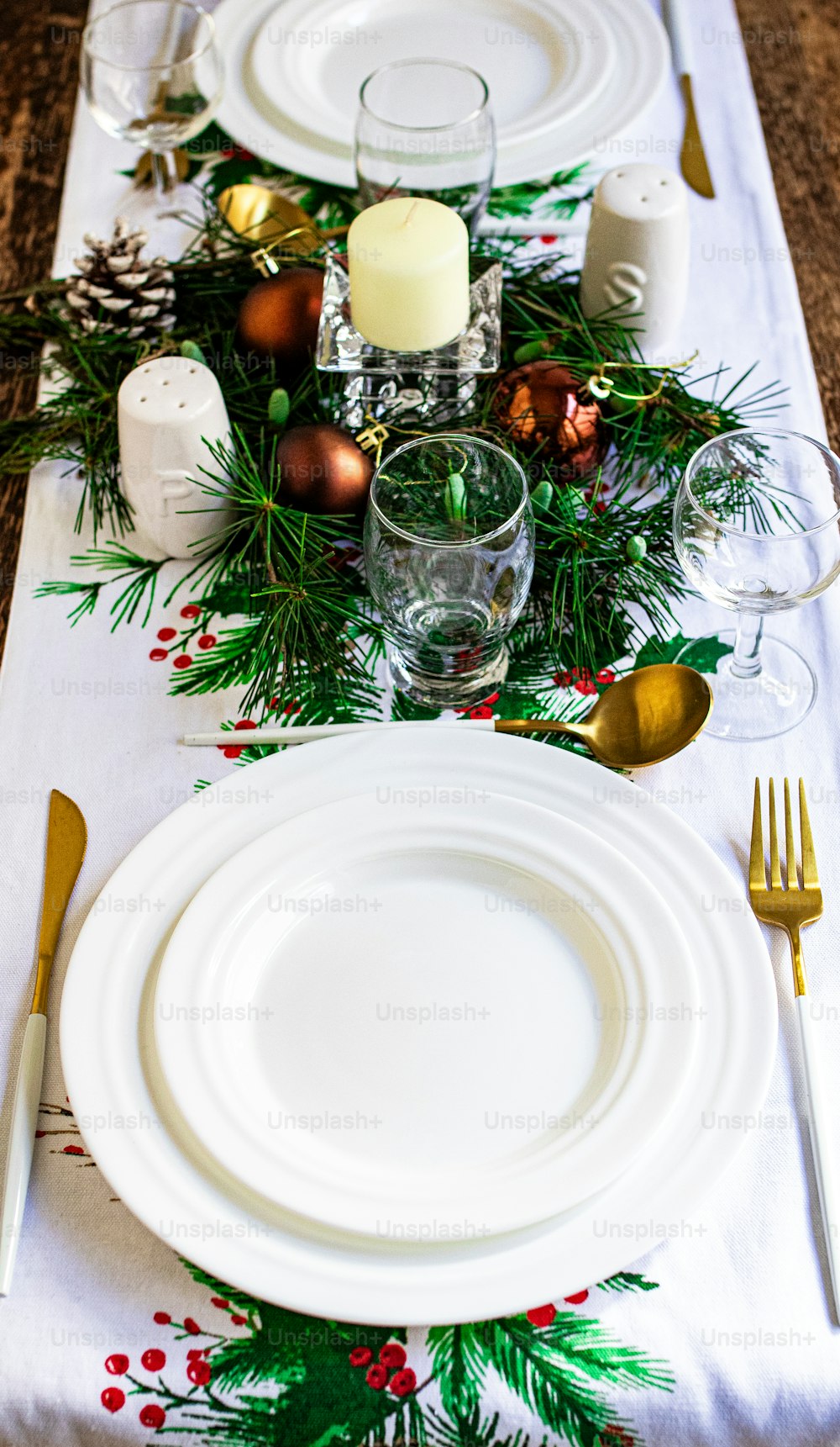 a table set for a holiday dinner with silverware and greenery