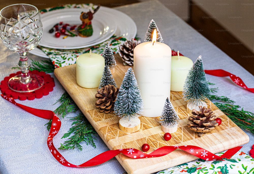 a table topped with a wooden cutting board covered in pine cones and candles