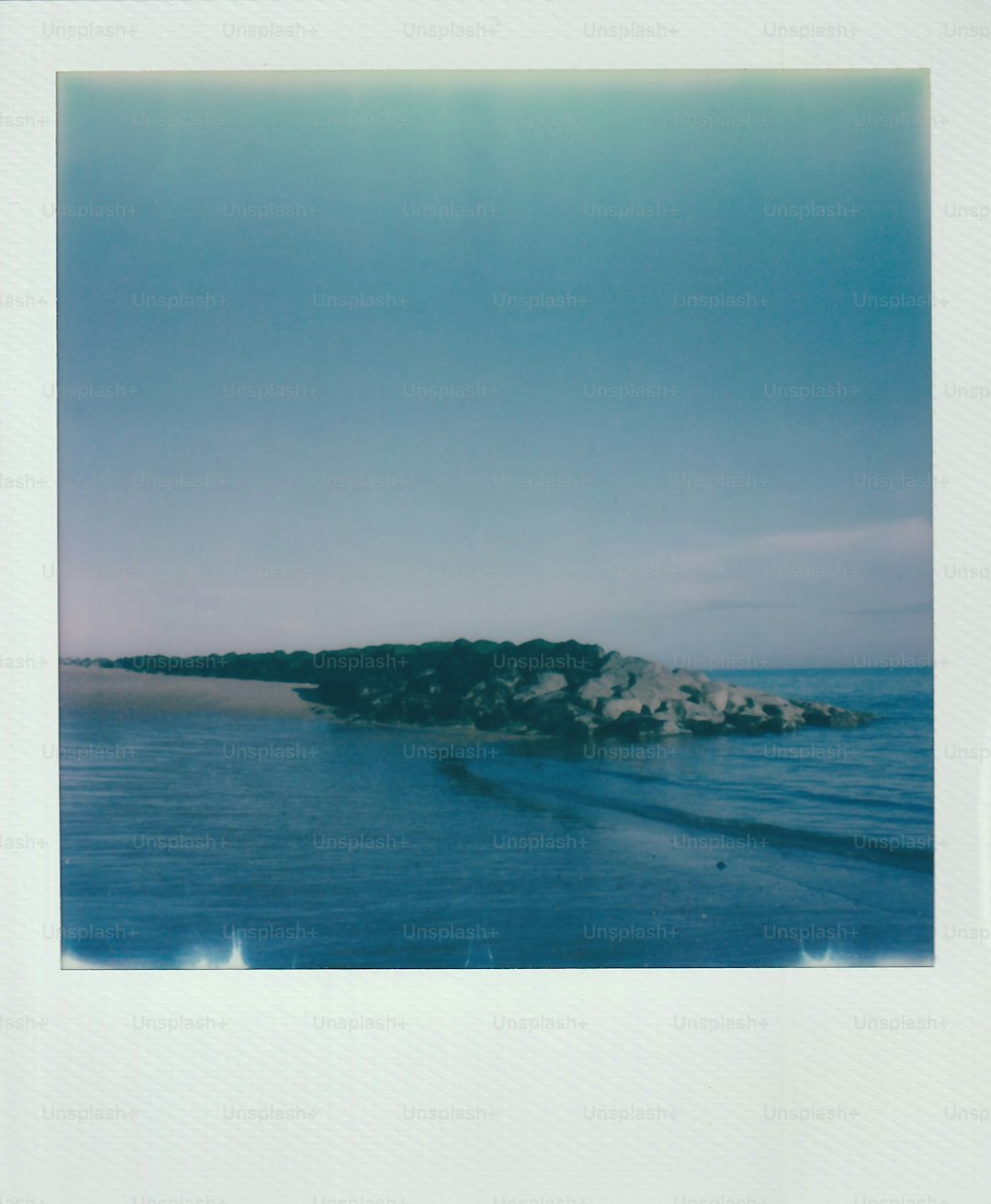 uma foto polaroid de uma praia com um afloramento rochoso