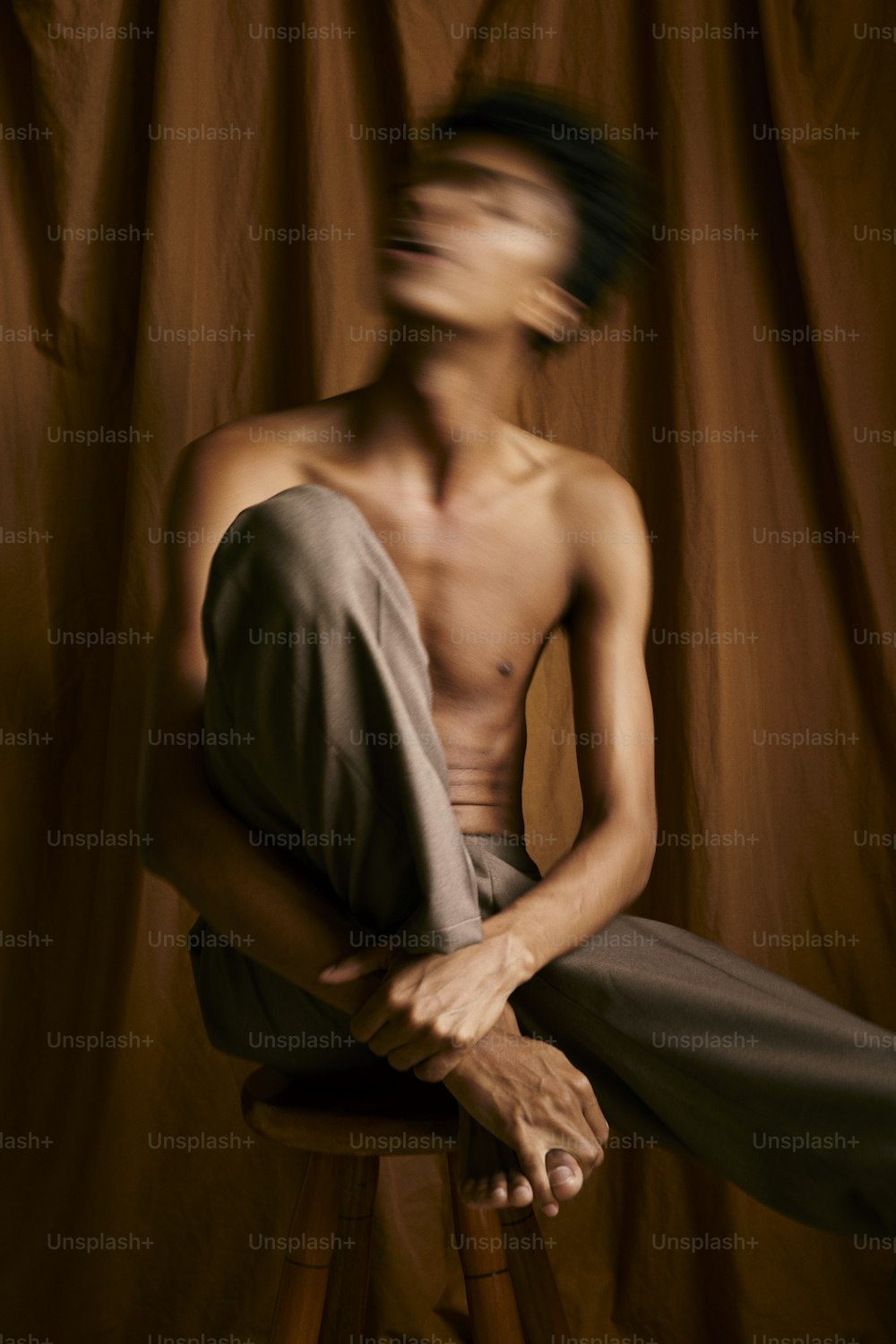 Un hombre sin camisa sentado en un taburete frente a una cortina