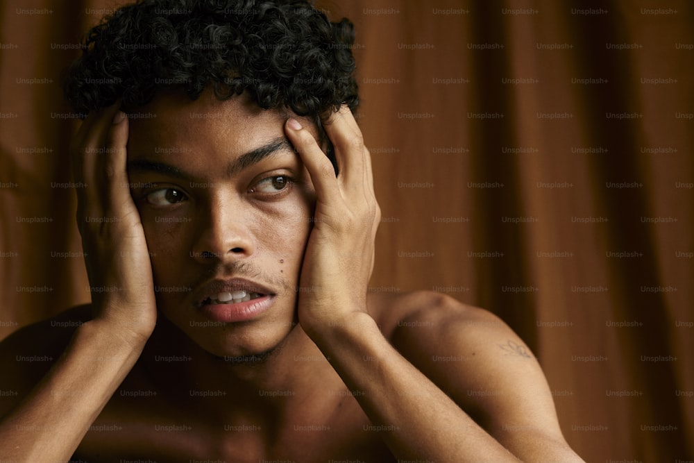 Un hombre sin camisa llevándose las manos a la cara