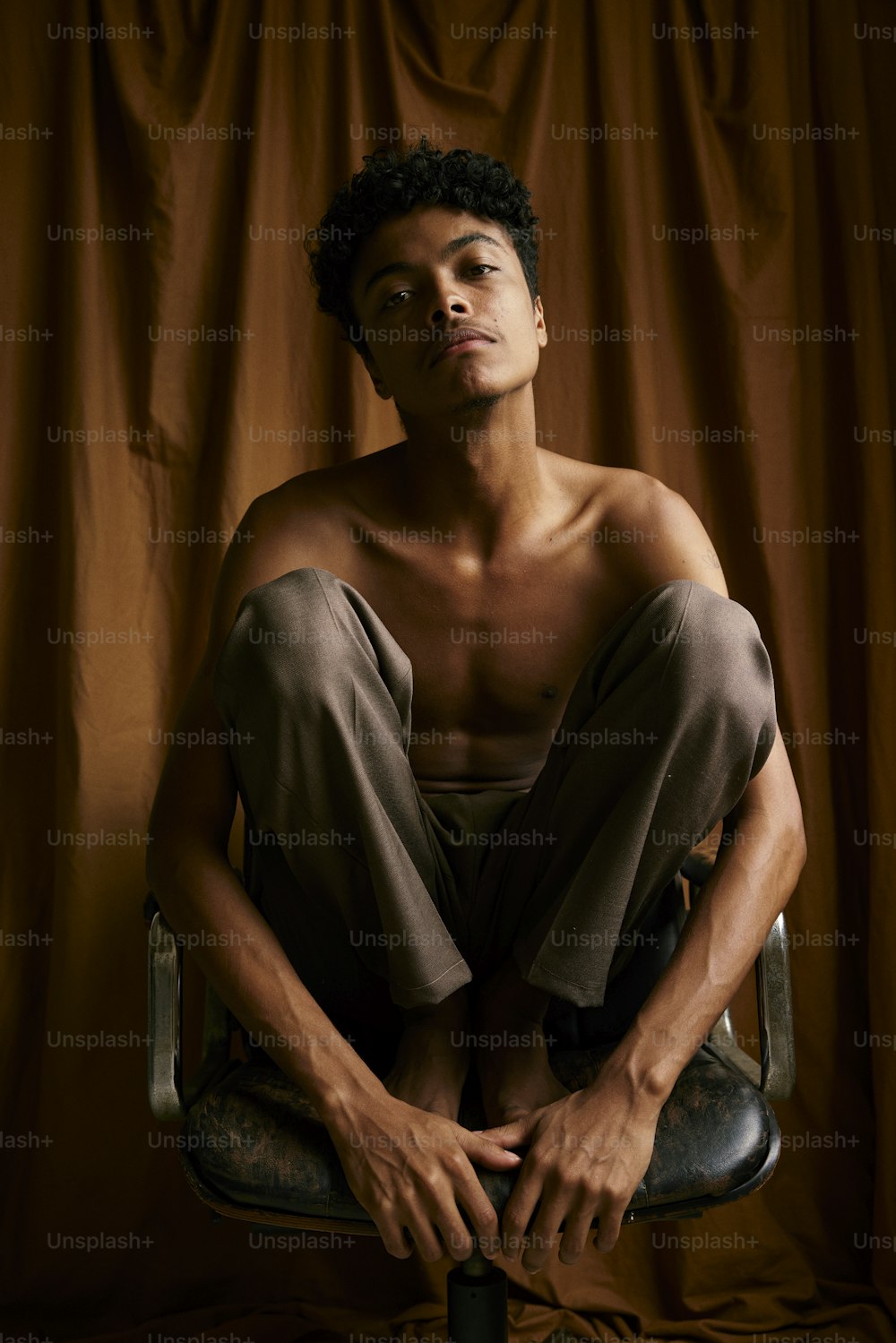 a shirtless man sitting on a chair in front of a curtain