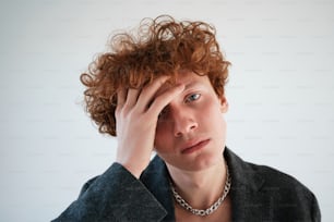 a young man with curly red hair holding his head