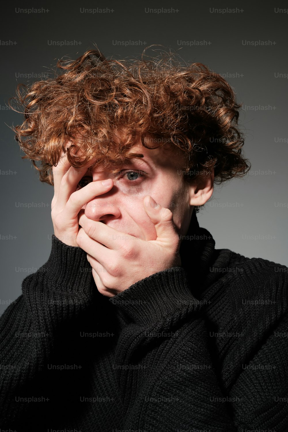 a man with curly hair covers his face with his hands