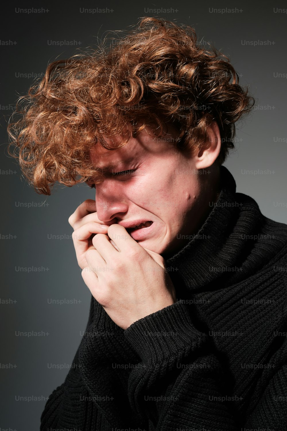 a man with curly hair covers his face with his hands
