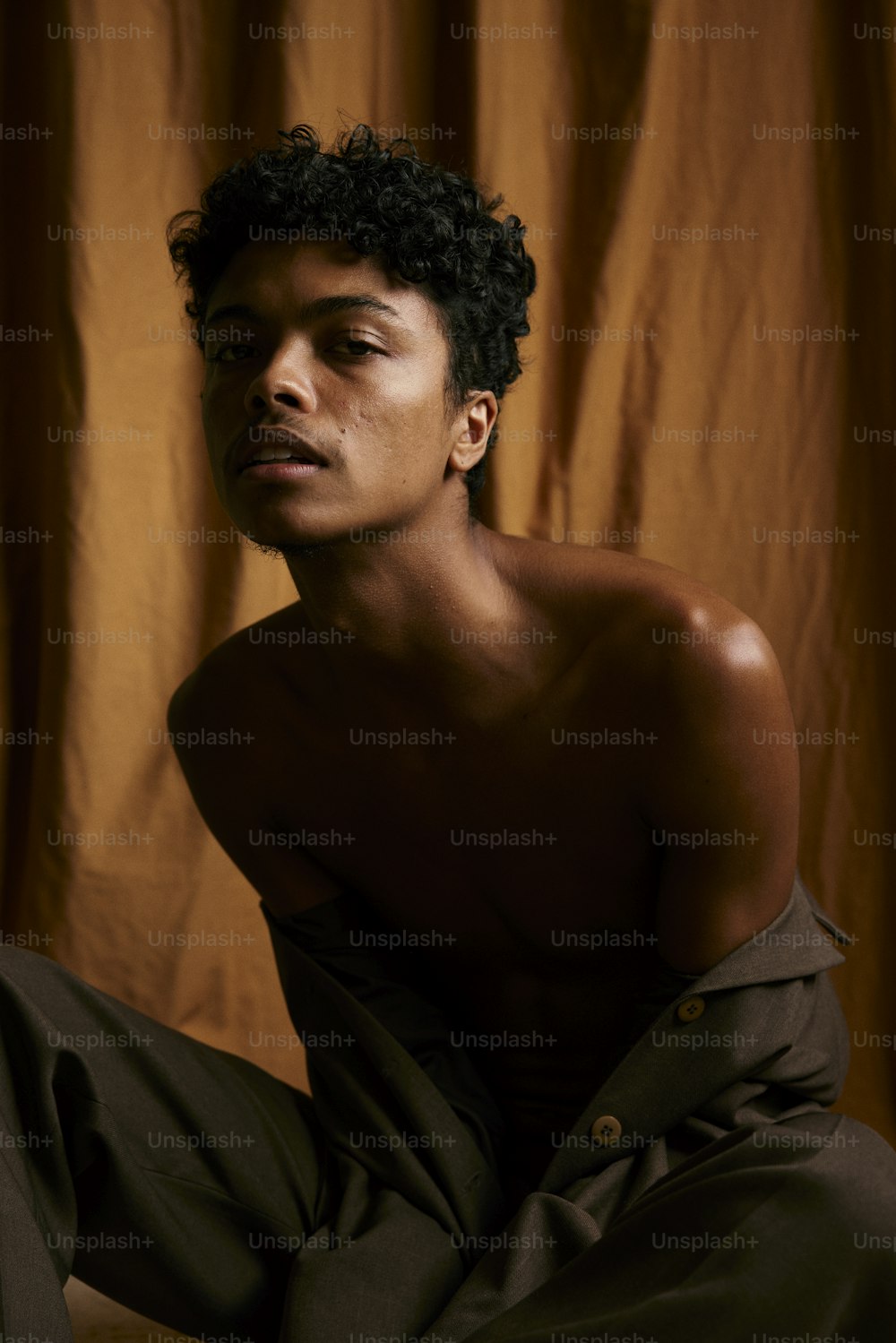 a shirtless man sitting on the floor in front of a curtain