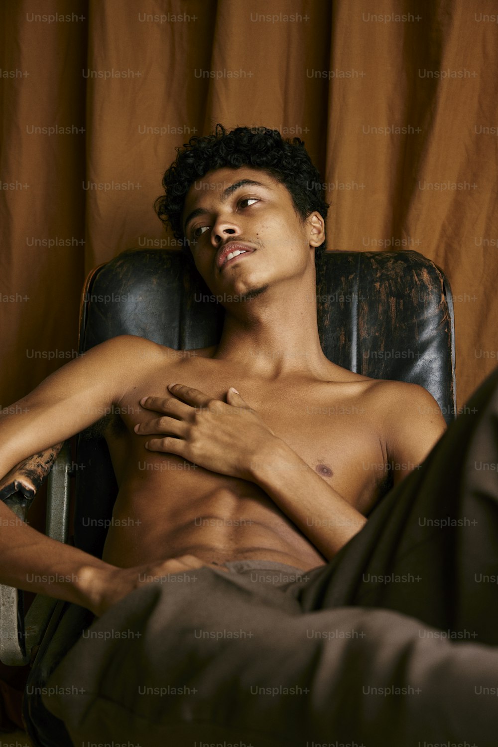 a shirtless man sitting in a chair with his hands on his chest