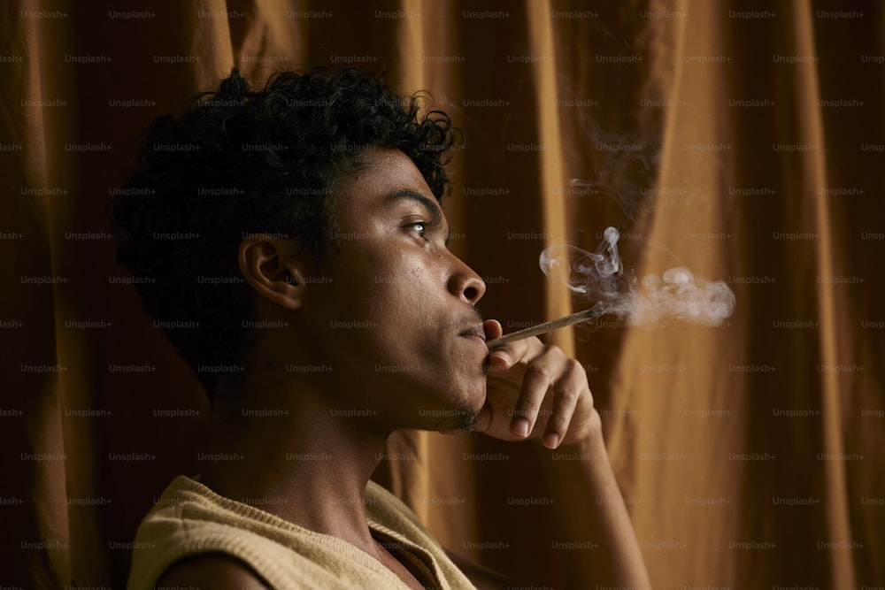 a young man smoking a cigarette in front of a curtain