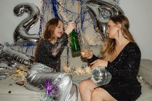 two women sitting on a couch with a bottle of champagne