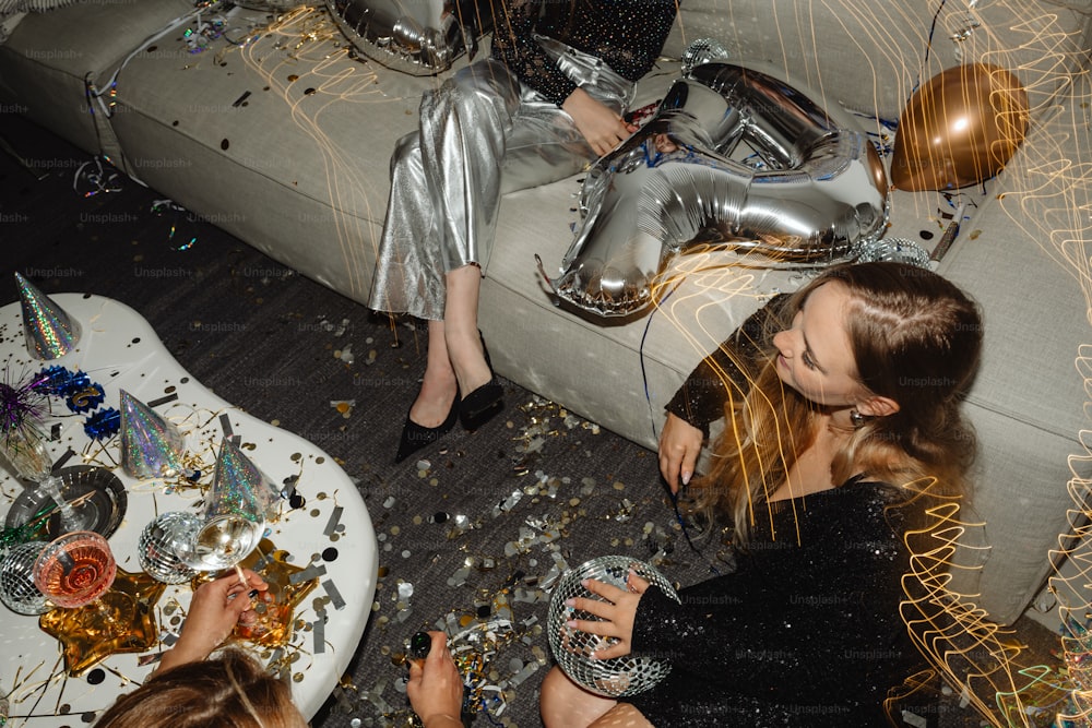 two women sitting on a couch surrounded by confetti and balloons