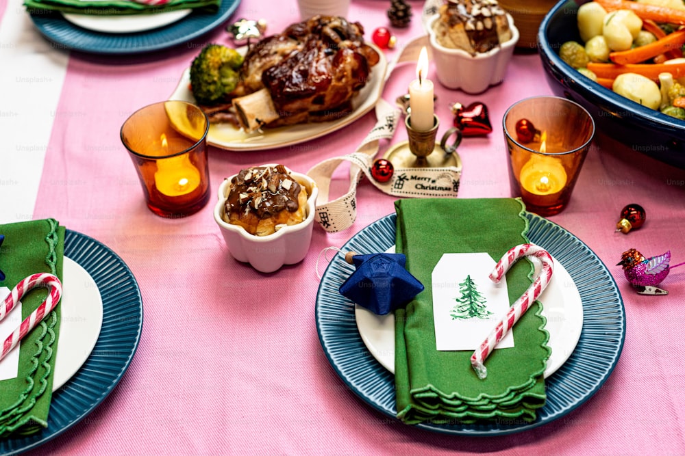 a table set for christmas dinner with a pink table cloth