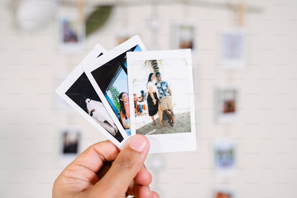 a person holding up four polaroid photos in front of a wall