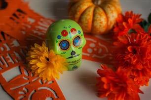 a green skull sitting on top of a table next to orange flowers