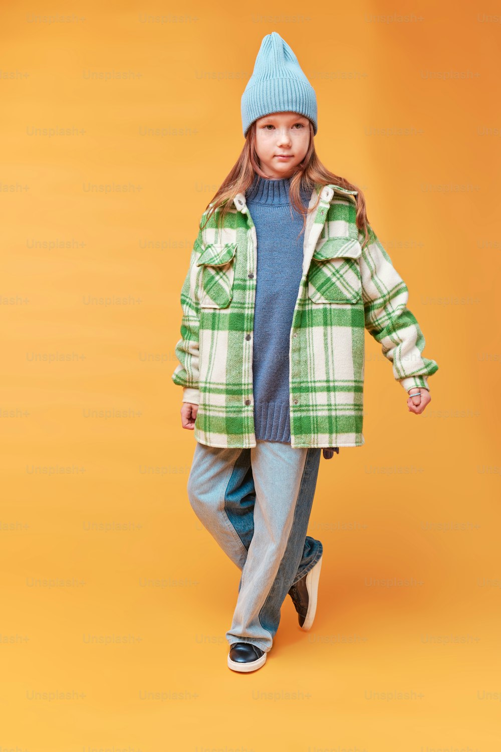 a little girl wearing a green plaid coat and a blue hat