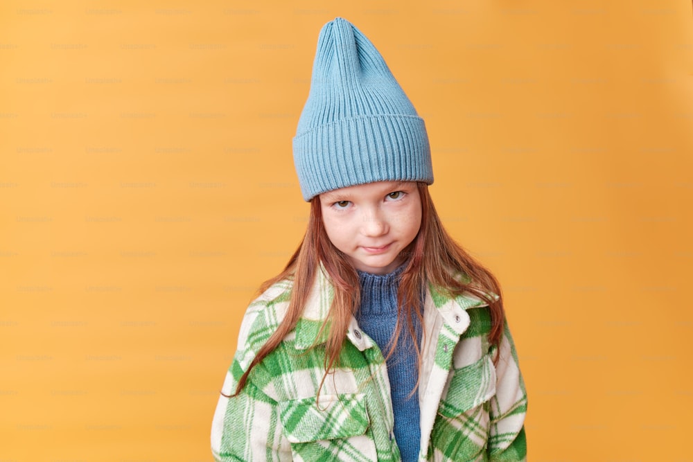 a young girl wearing a blue hat and green jacket