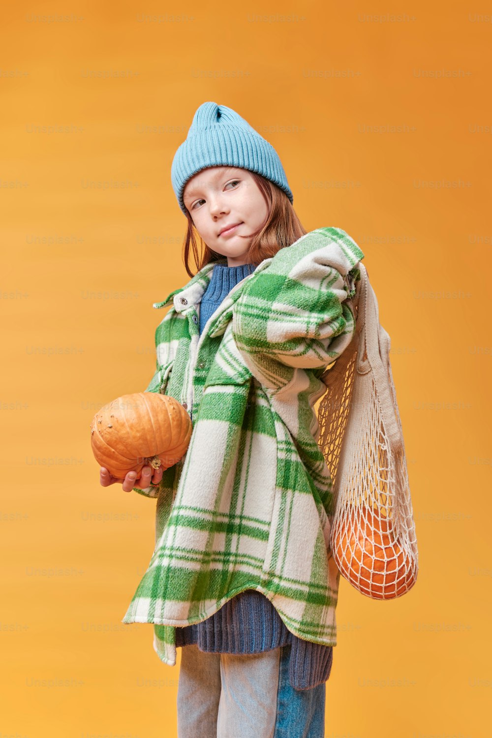 a little girl holding a pumpkin and a bag