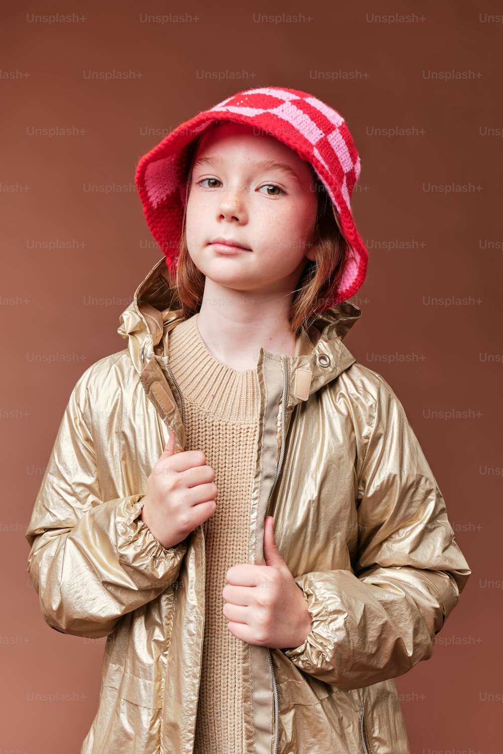 a little girl wearing a gold jacket and a red hat