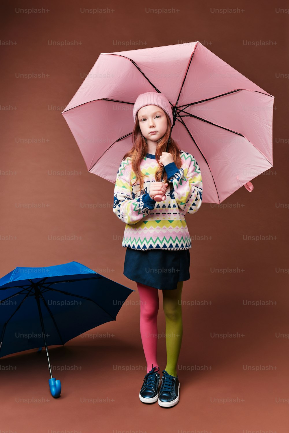 a little girl holding a pink umbrella next to a blue umbrella