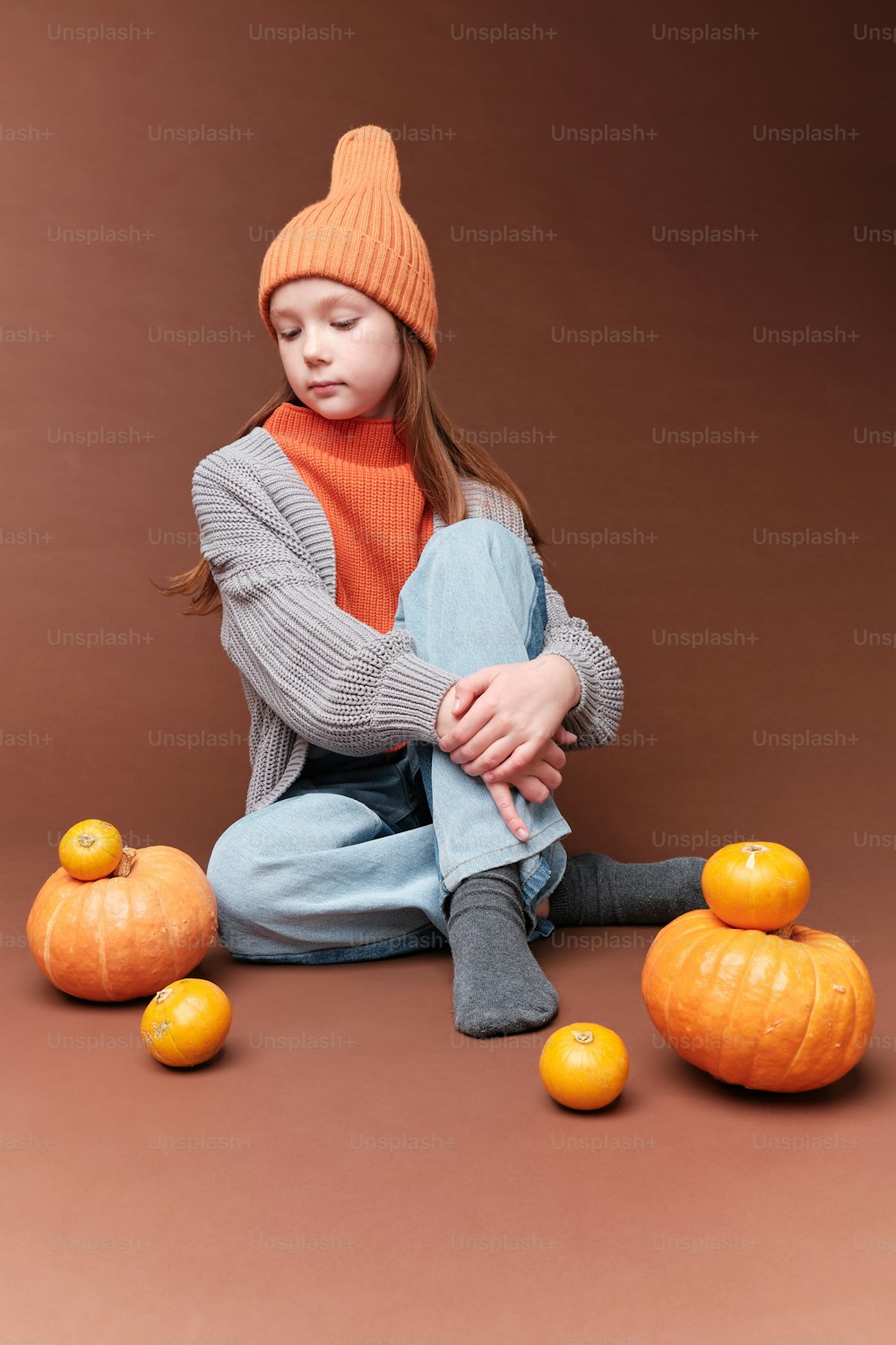 a young girl sitting on the ground surrounded by pumpkins