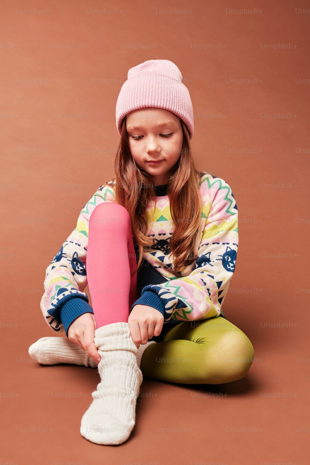 a little girl sitting on the ground with a pink object