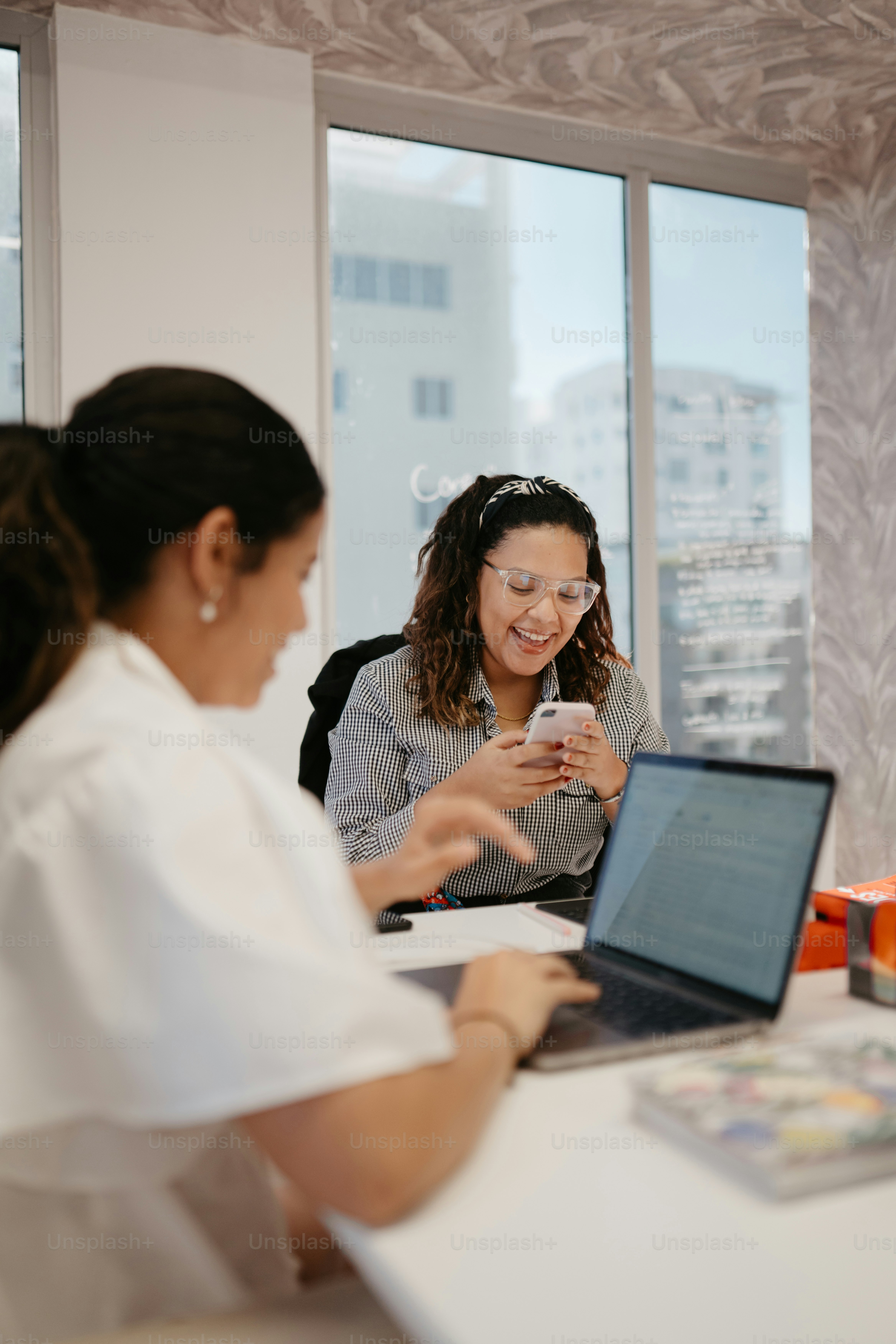 two women sitting at a table looking at a cell phone