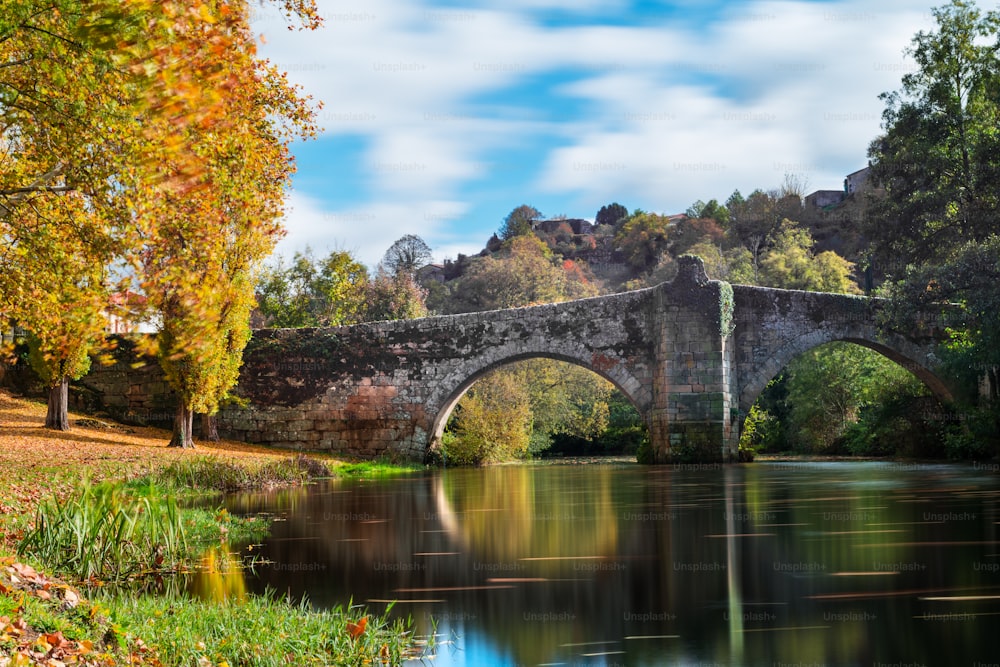 가을 단풍과 중세 로마 다리는 갈리시아의 Allariz 마을, Ourense의 물에 반영되었습니다.