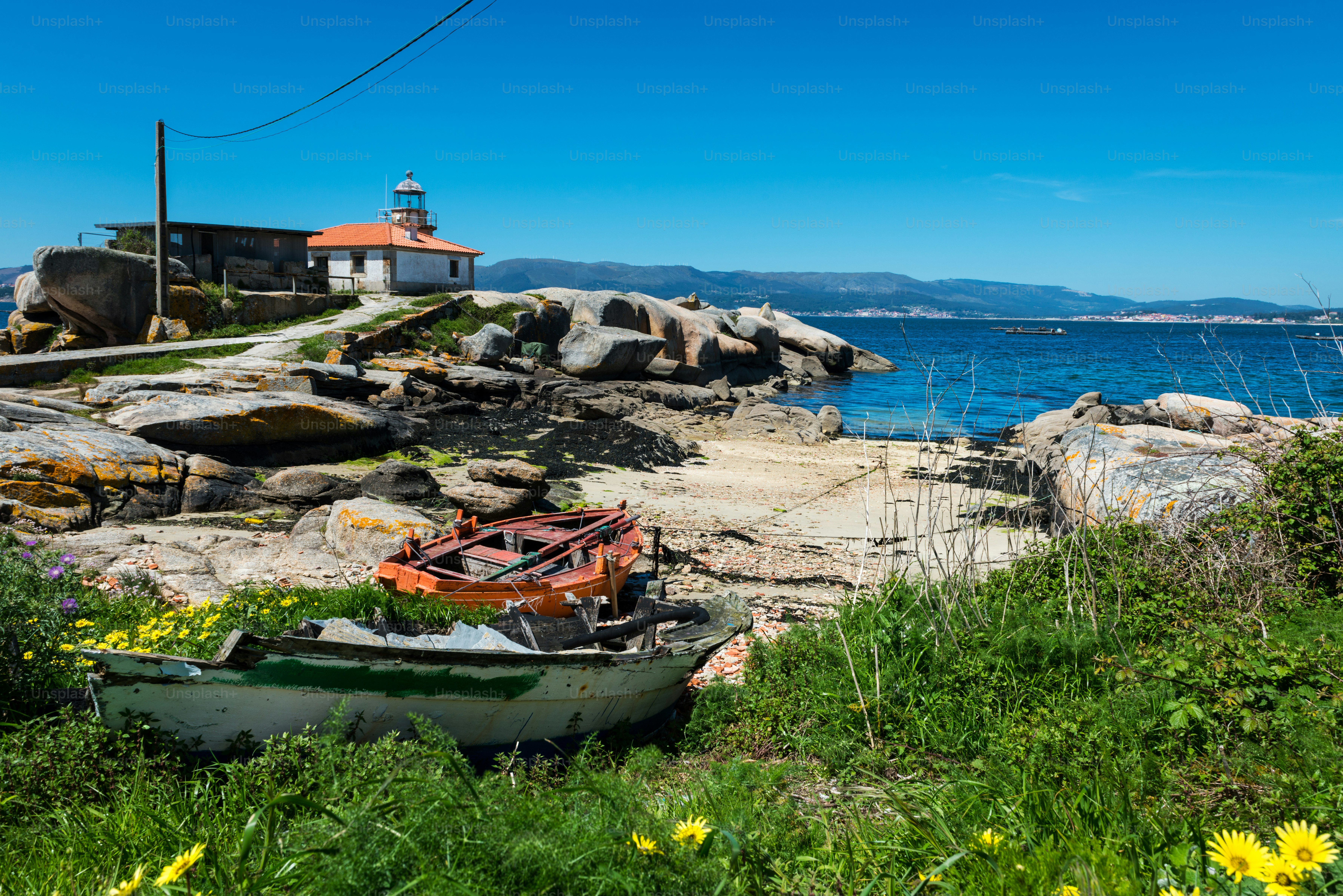 Petit phare ancien sur l’île d’Illa de Arousa dans les Rias Baixas en Galice, en Espagne, avec quelques bateaux en bois abandonnés au premier plan.