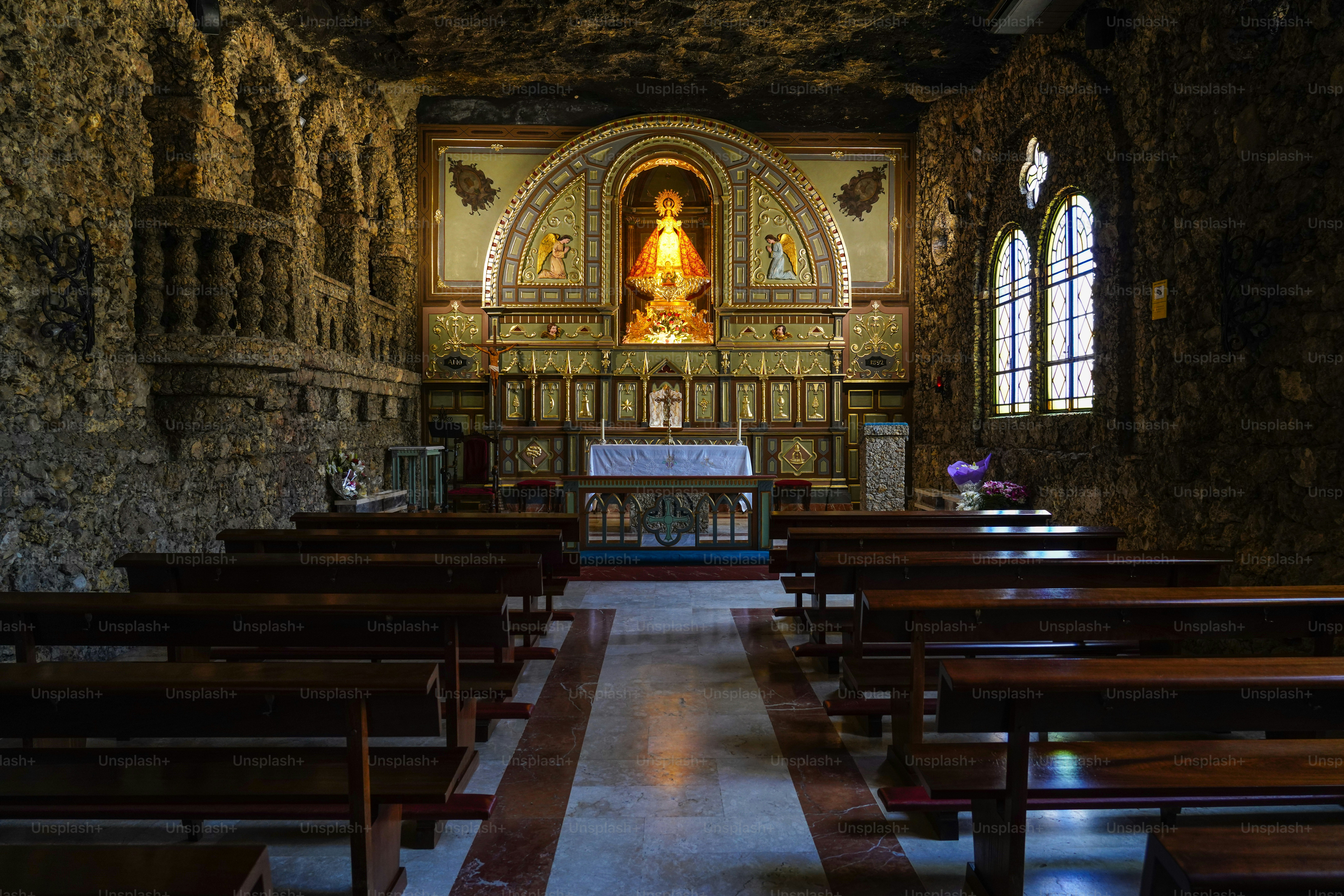 An ornate altar and wooden pews inside a rustic stone church with arched windows