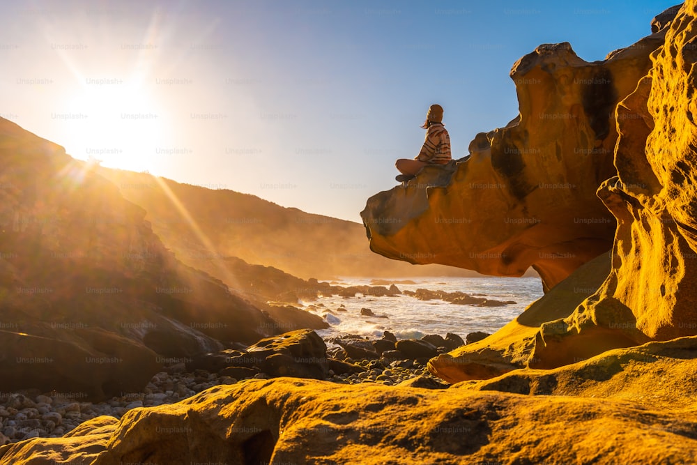 A young woman relaxed at sunset in the cove of stones in the Jaizkibel mountain in the town of Pasajes, Gipuzkoa. Basque Country