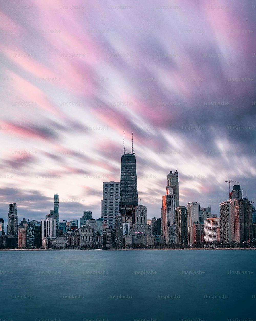 Una vista impresionante de la Torre Willis en Chicago con agua azul silenciosa bajo un cielo nublado rosado al amanecer