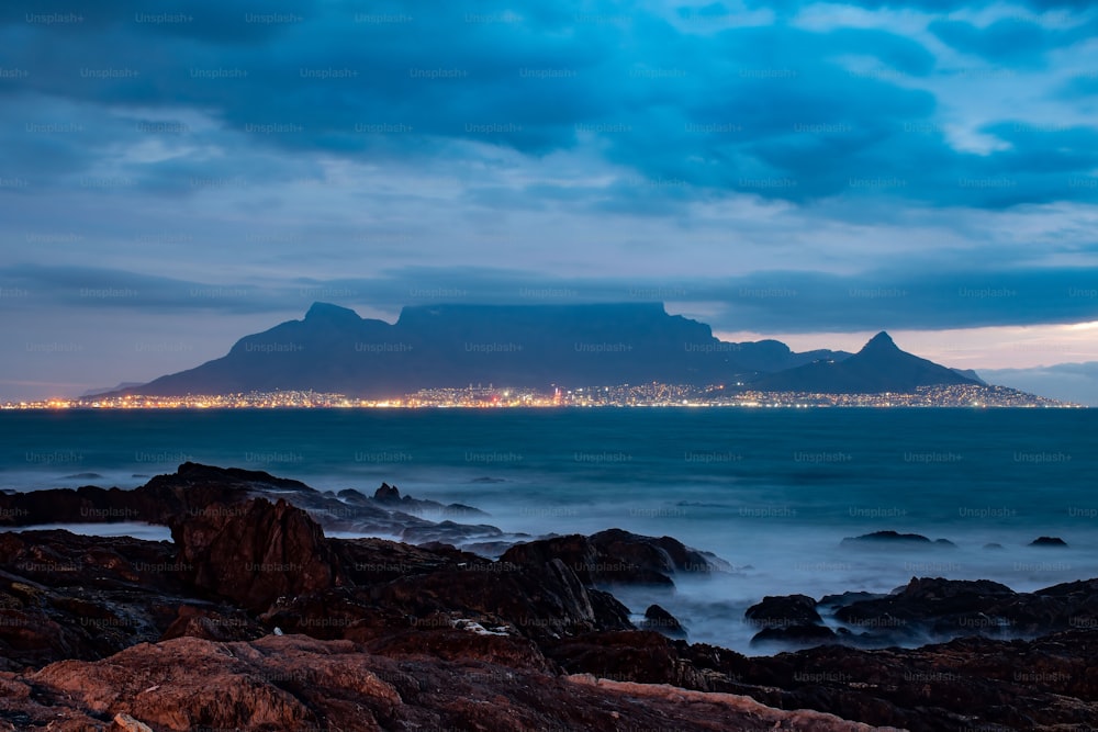 Eine wunderschöne Landschaft mit steinigen Stränden mit Blick auf den Tafelberg und Kapstadt an einem bewölkten Abend