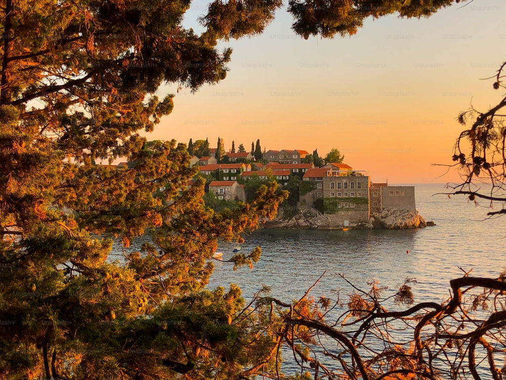 A scenic view of Sveti Stefan unfolding behind the trees in autumn foliage during sunset