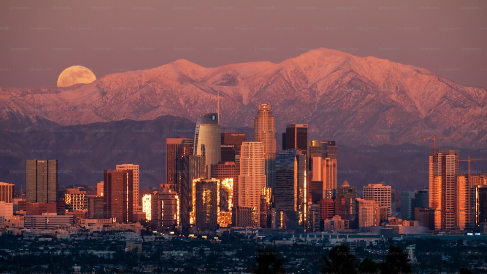 Der Vollmond, der während des Sonnenuntergangs über den schneebedeckten San Gabriel Mountains in Los Angeles aufgeht